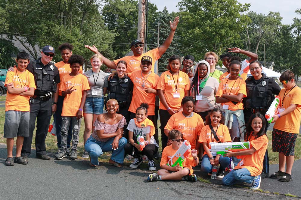 LifeCamp makes an impact on kids in our community. Counselors, community police officers, and Urban Alliance staff gather together with campers where bright orange shirts for a group photo.