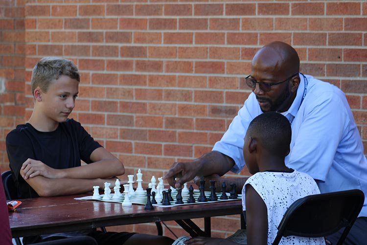 A volunteer teaches two neighborhood children how to play chess.