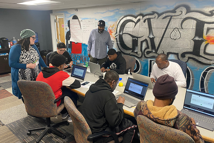 Momentum participants work on laptops together while the instructors look on.